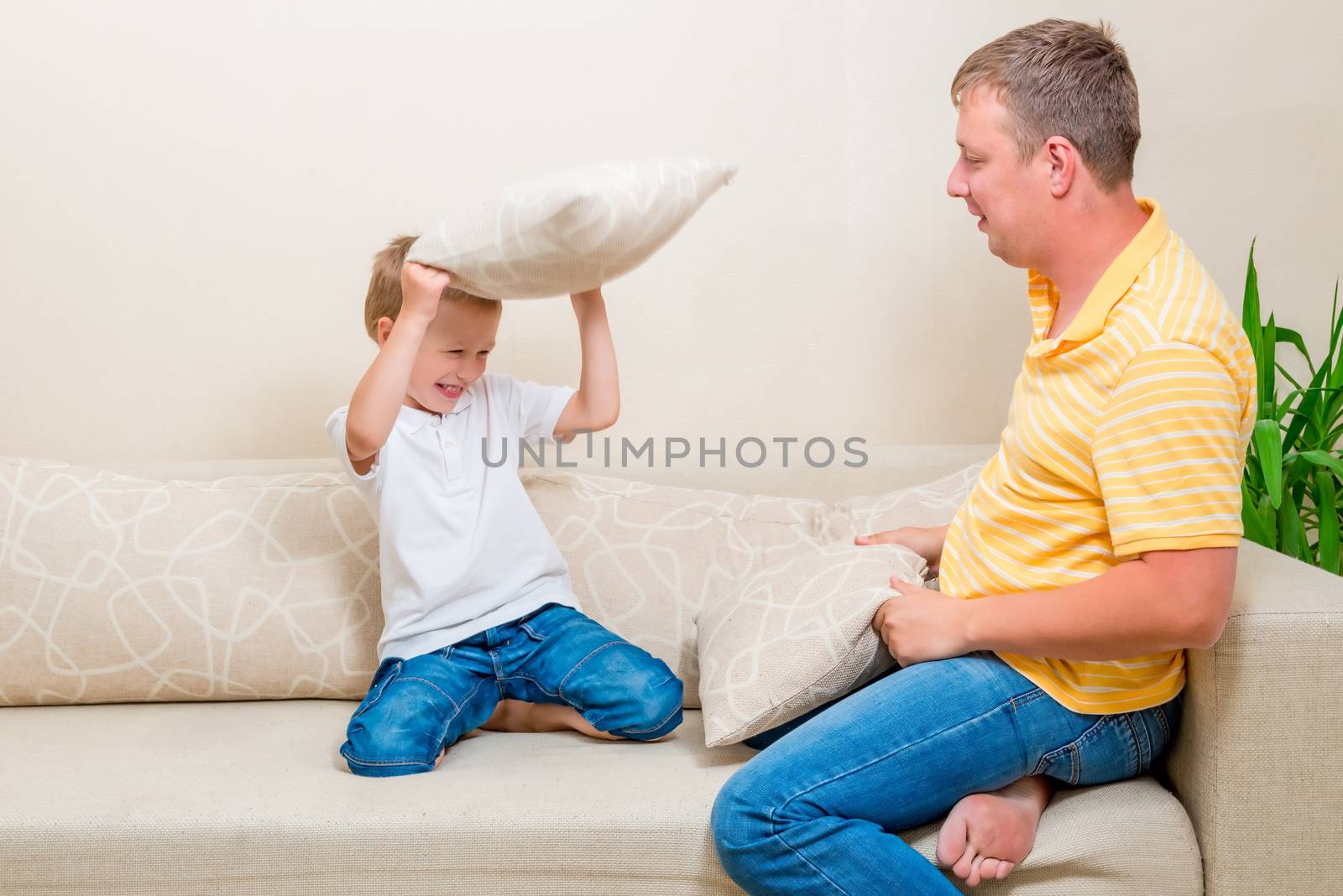 father and son fighting pillows on the couch by kosmsos111