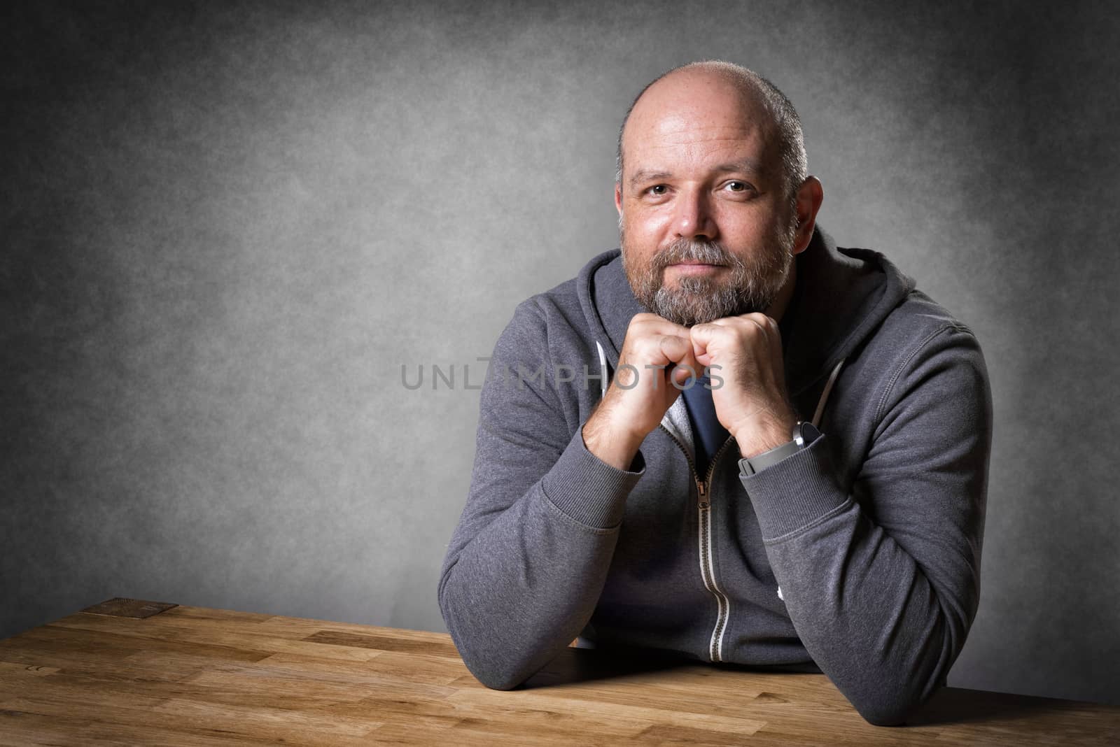 Portrait of a friendly looking, balding and unshaven man sitting on a wooden table
