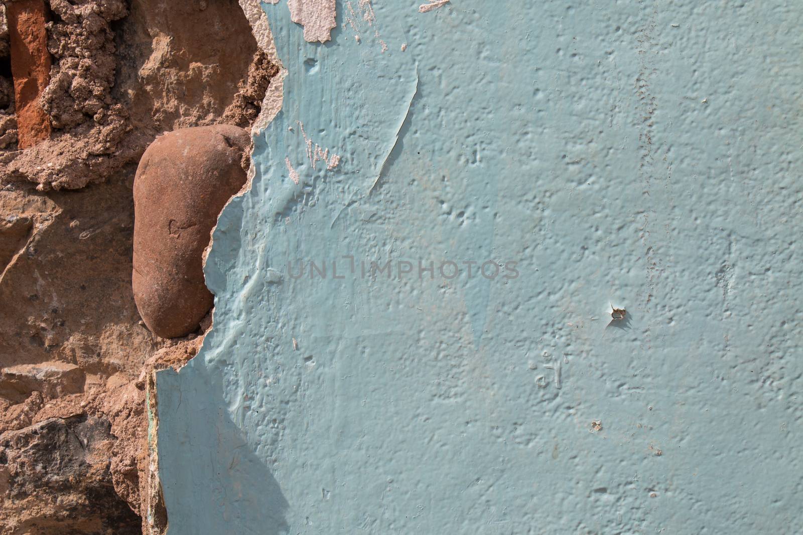 Broken blue painted wall, visible concrete base together with a big stone.