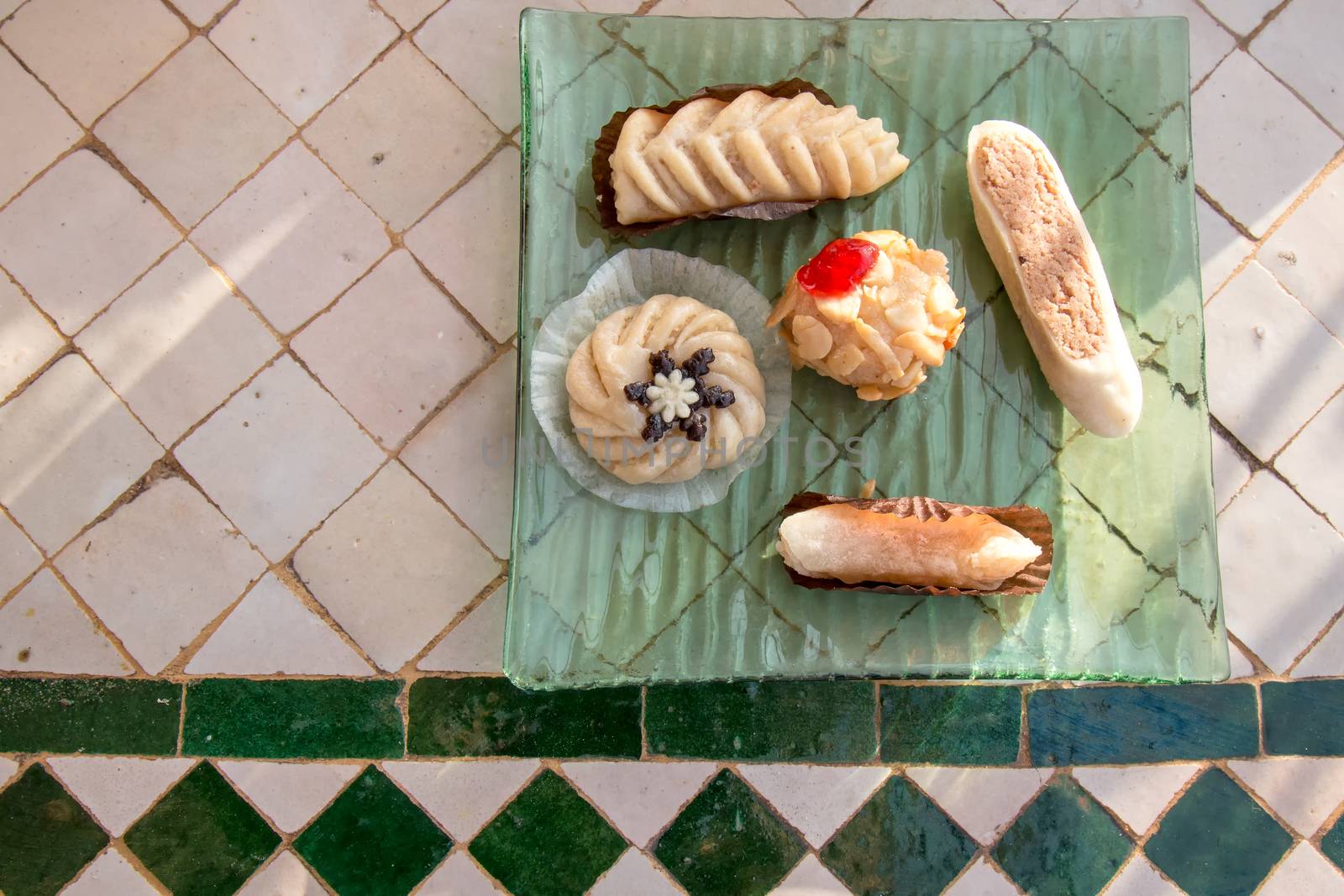 Like small jewels, assortment of traditional arabian sweets, served on a green plate and mosaic table.