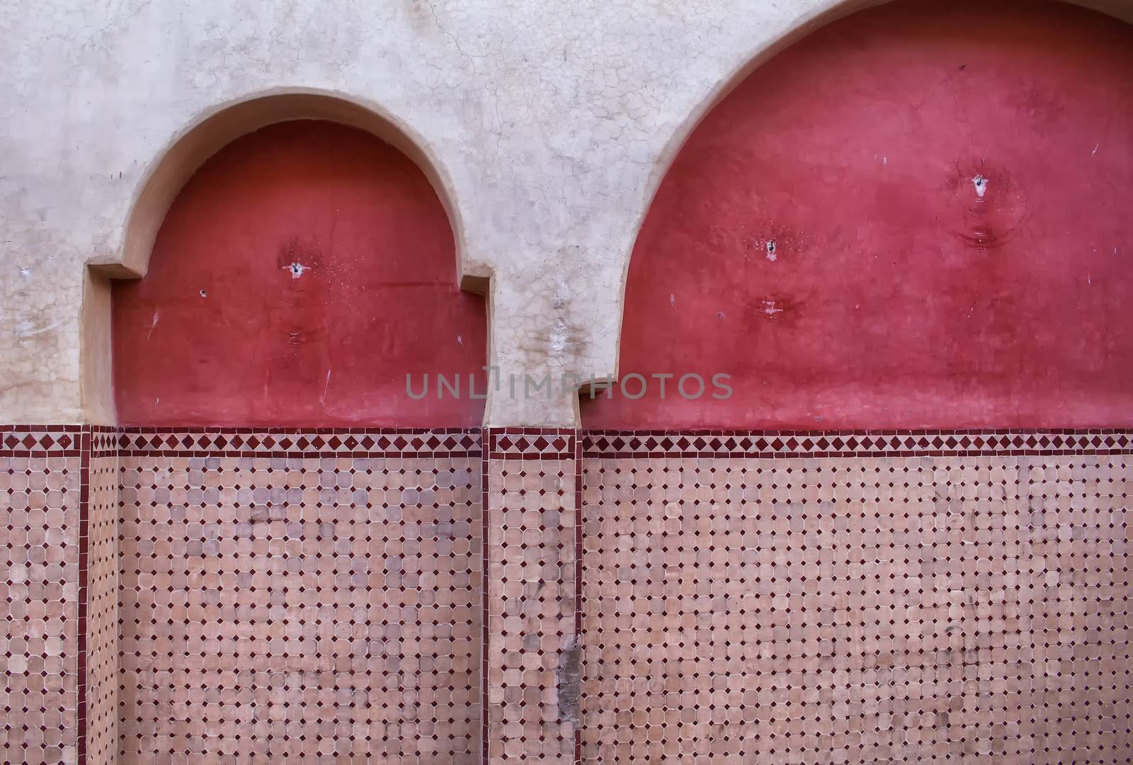 Part of a facade with arcs, traditional in arabian architecture. Partly painted red, partly with tiles detail.