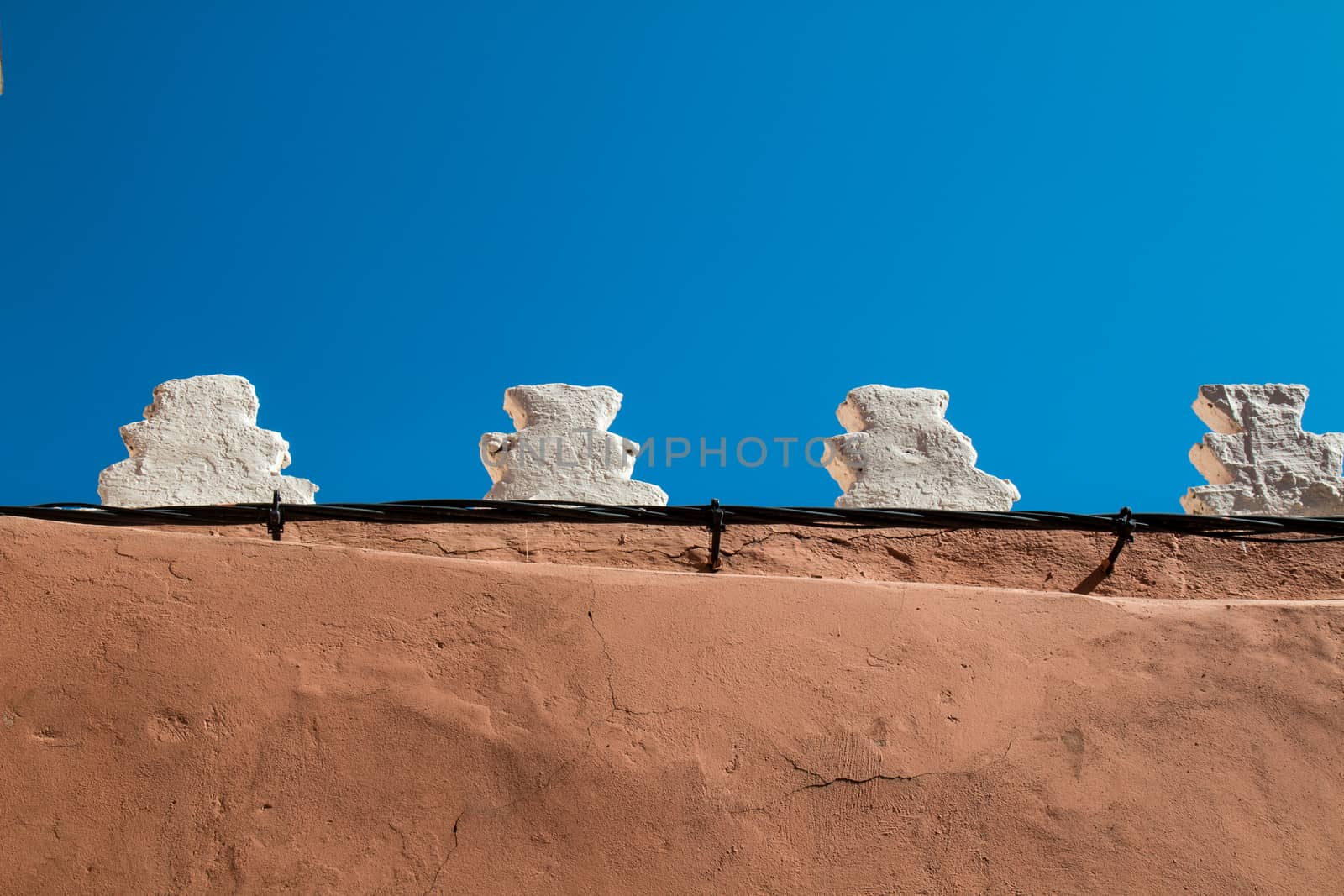 Sand color of the fence, white traditional details on the edge. Bright blue sky.