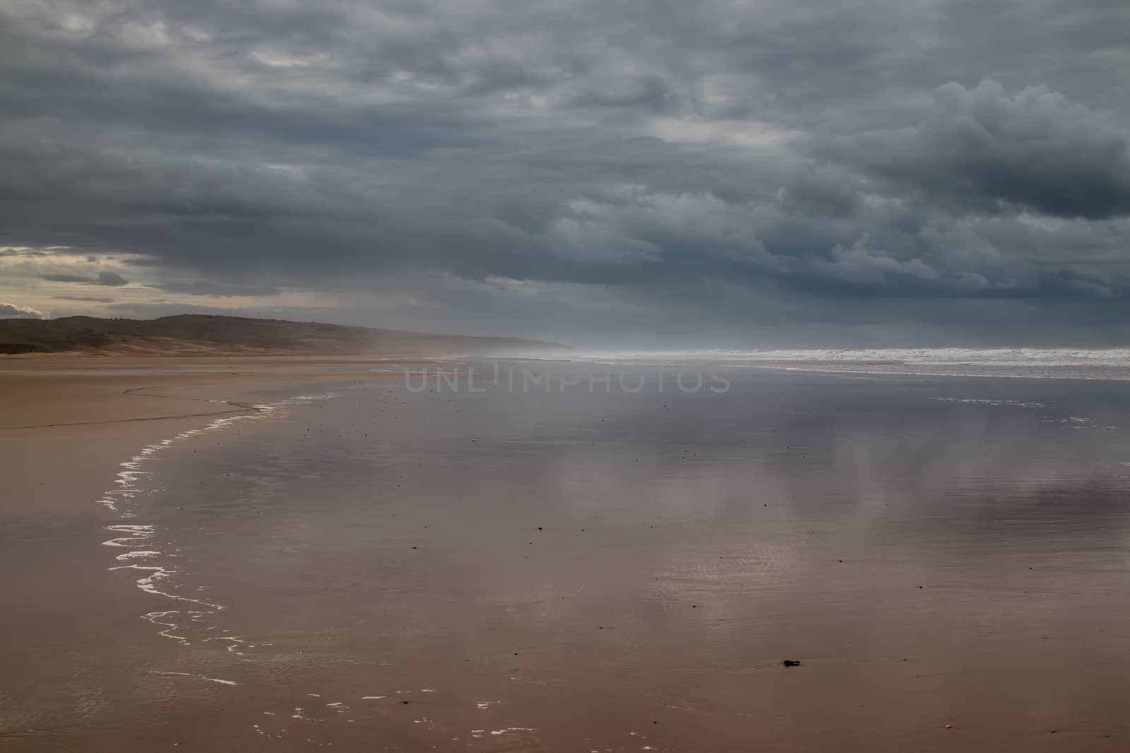 Stormy weather with heavy clouds. Beach with a wavy water of the Atlantic ocean during a tide. Mountain in the background.