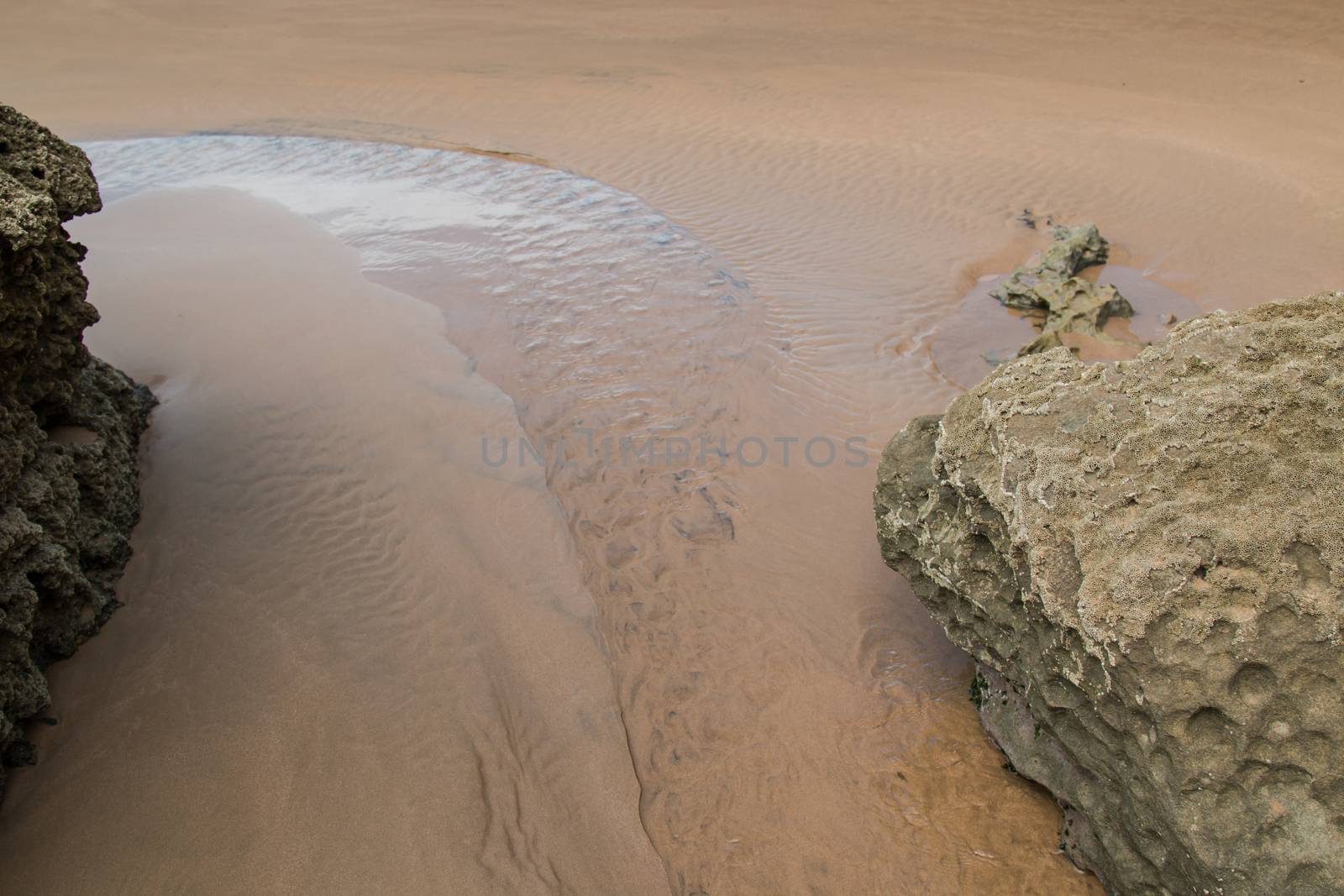 Golden sand with puddles filled with water from the ocean, after a tide. On the sides rocks on the beach. Atlantic ocean coast, Morocco.