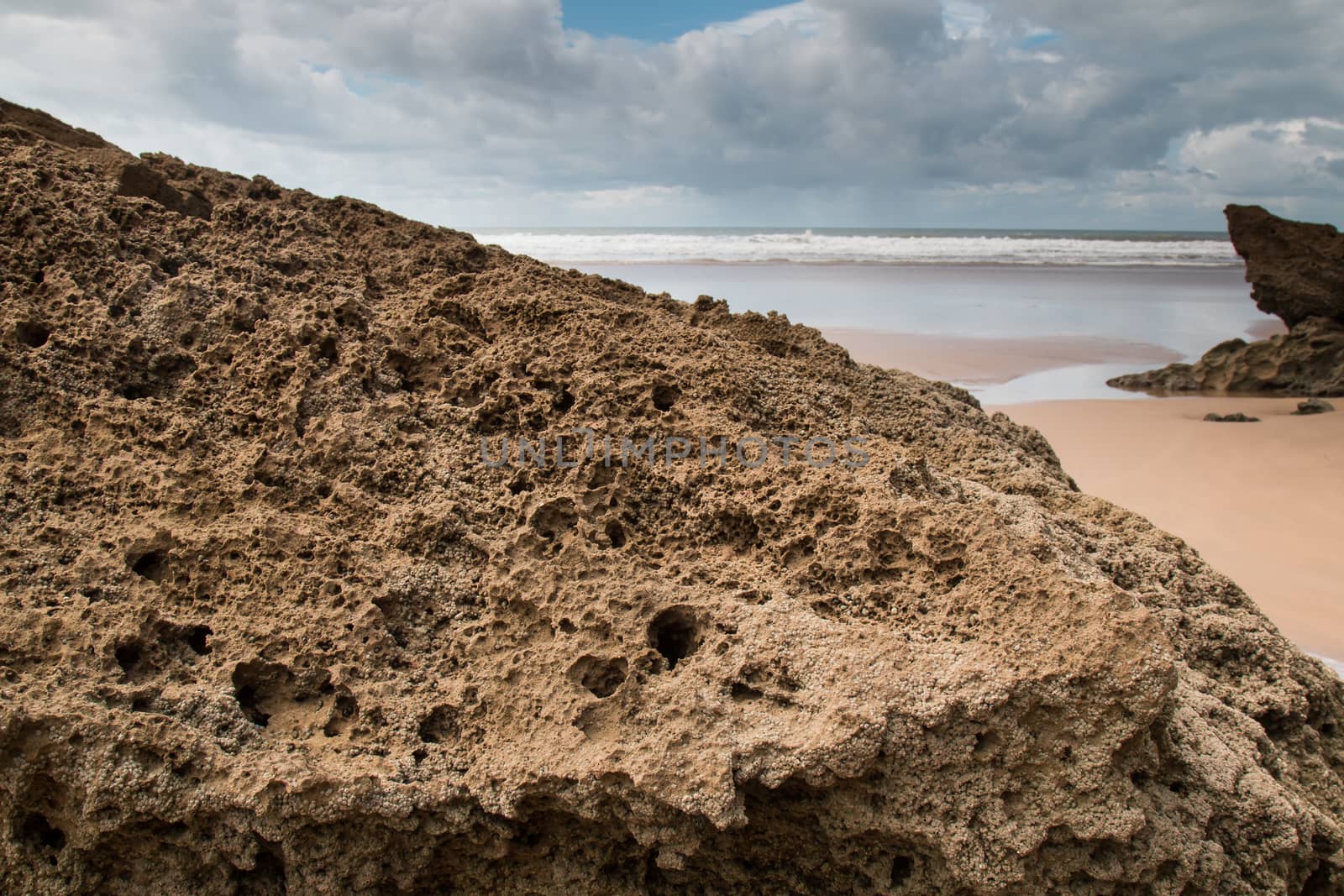 Rocks on the sandy beach in the foreground. Windy autumn day with many clouds. Waters of Atlantic Ocean in the background. Moulay Bouzerktoun, Morocco.