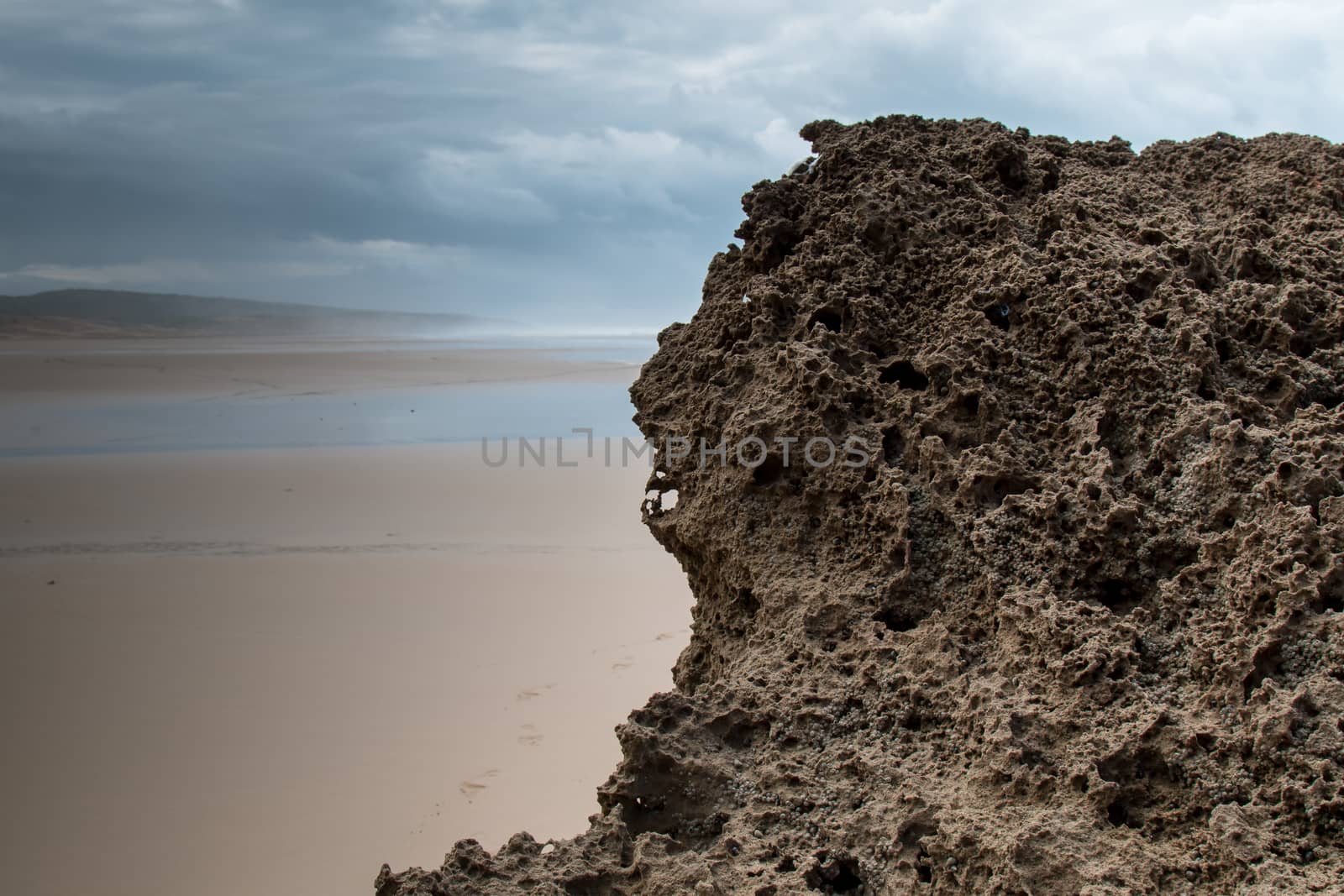 Rocks on the sandy beach in the foreground. Windy autumn day with many clouds. Waters of Atlantic Ocean in the background. Moulay Bouzerktoun, Morocco.