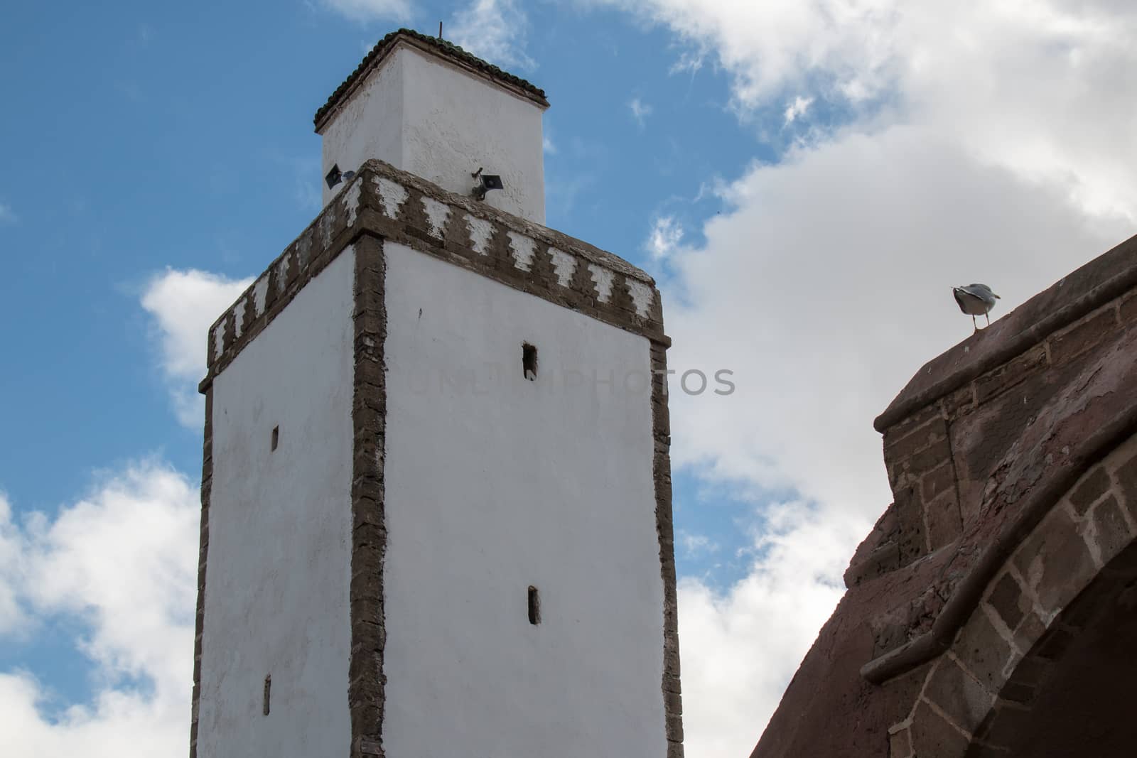 White facade of a mosque with bricks lining of the minaret. Cloudy sky.