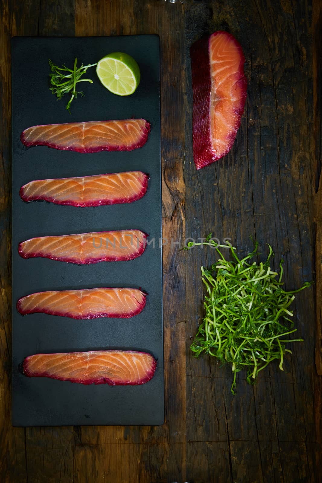 Sliced salmon fillet, sauteed with beetroot juice over black slate surface. Top view