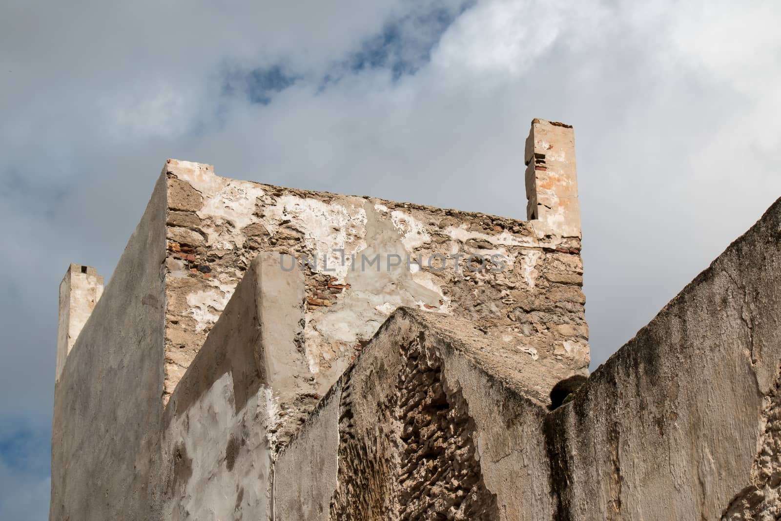 Very old facade of a building in traditional moroccan style, with visible bricks base. Cloudy stormy sky.