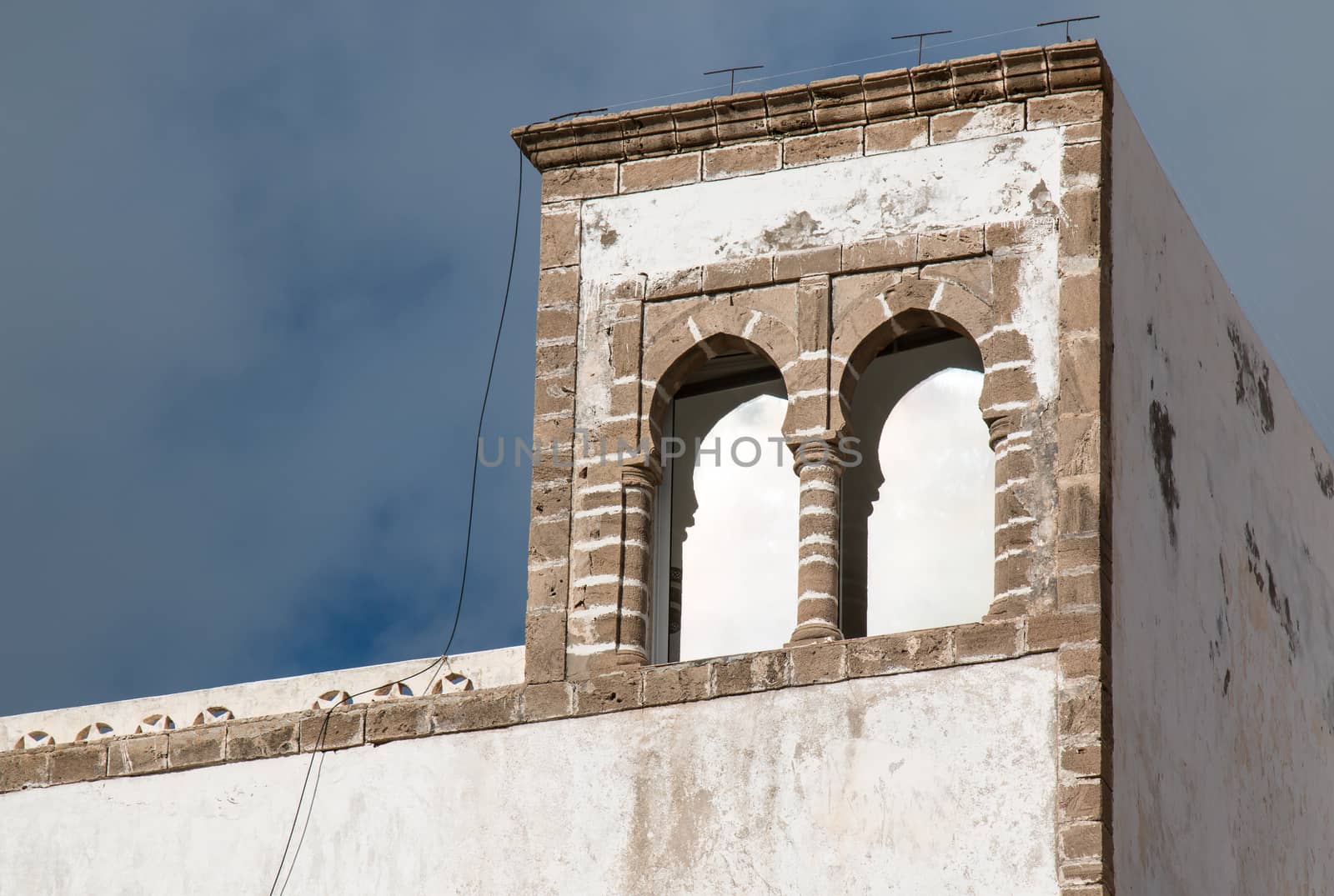 Building with white old facade and with stone details, framing also the arcs of the window. Stormy sky in the background.