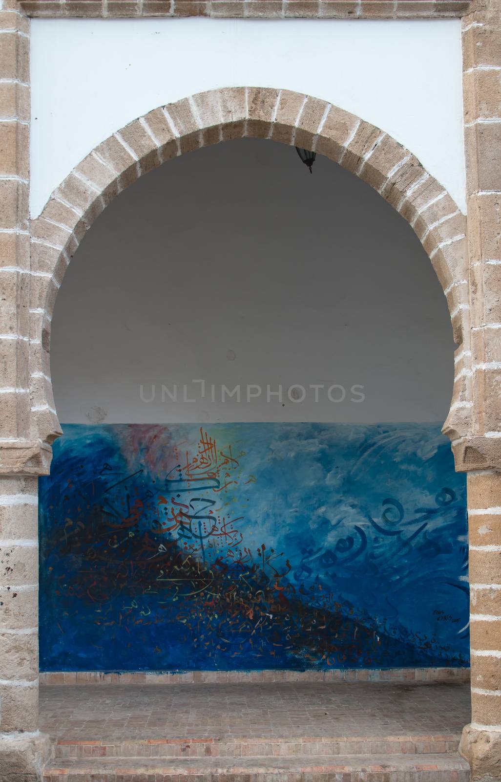 Building with white facade and a traditional arch. Colorful graffiti in the background. Essaouira, Morocco.