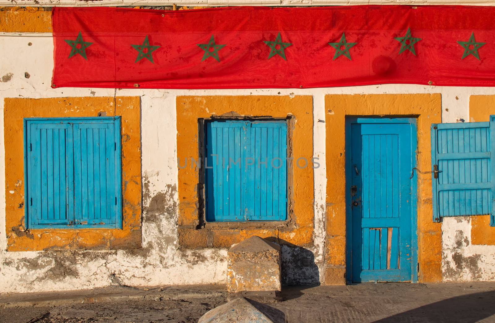 Blue shutters of the windows and blue door with orange frames. Old house in Essaouira. Stripe of long moroccan flag.