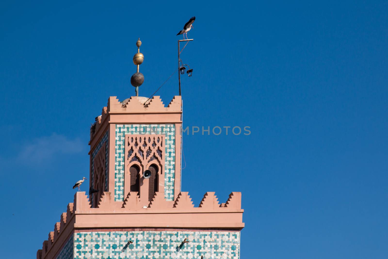 Detail of the minaret - tower of a mosque. Two birds - storks. Bright blue sky.