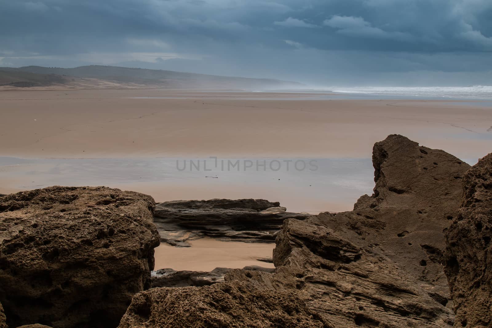 Cloudy day on a sandy beach of Atlantic Ocean in Morocco. Big rocks in the foreground.