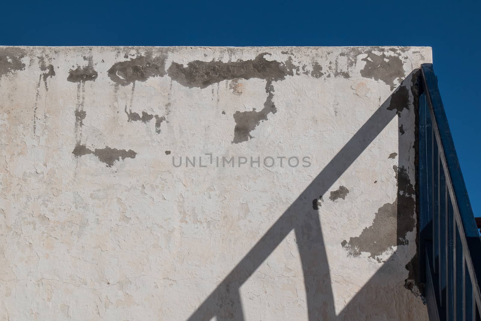 Old wall in the exterior, shadow of a handle of the stairs. Bright blue sky.
