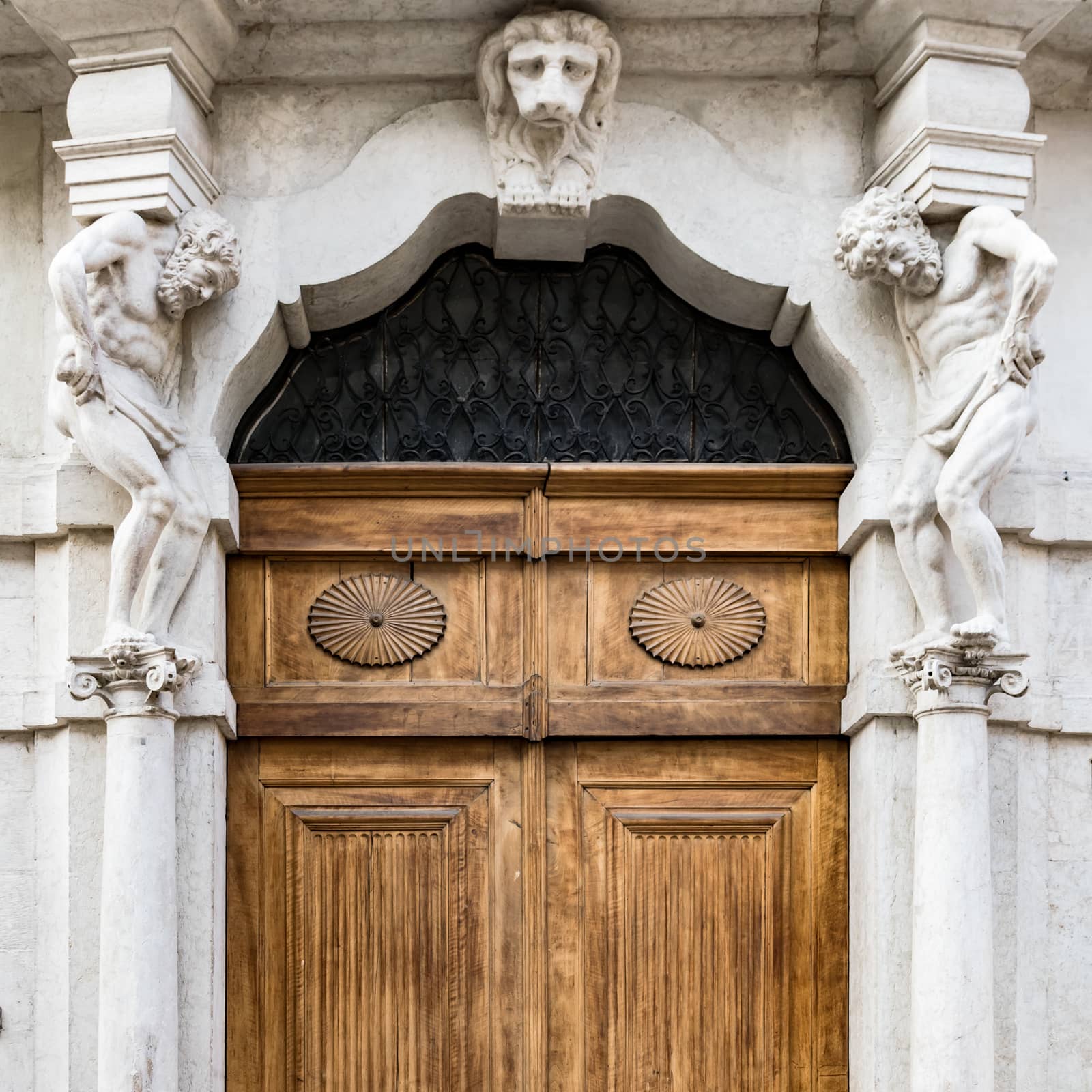 Old white stone entrance and wooden portal with statues that support the side columns.