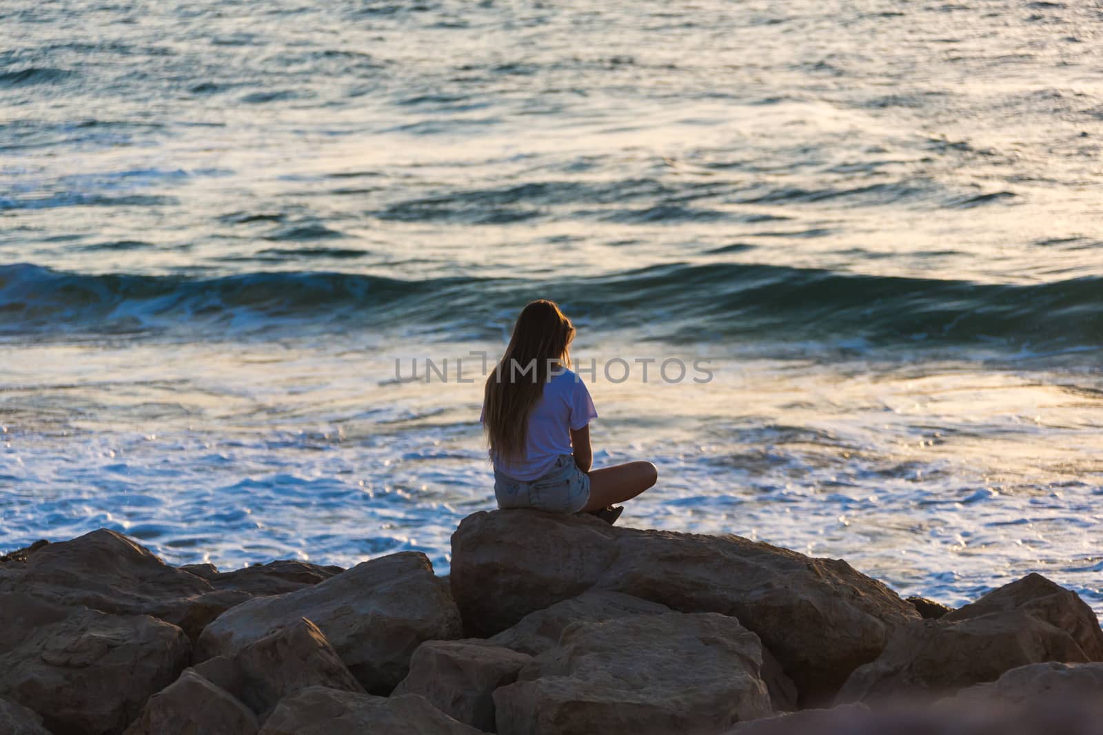 young woman sitting on the rocky seashore