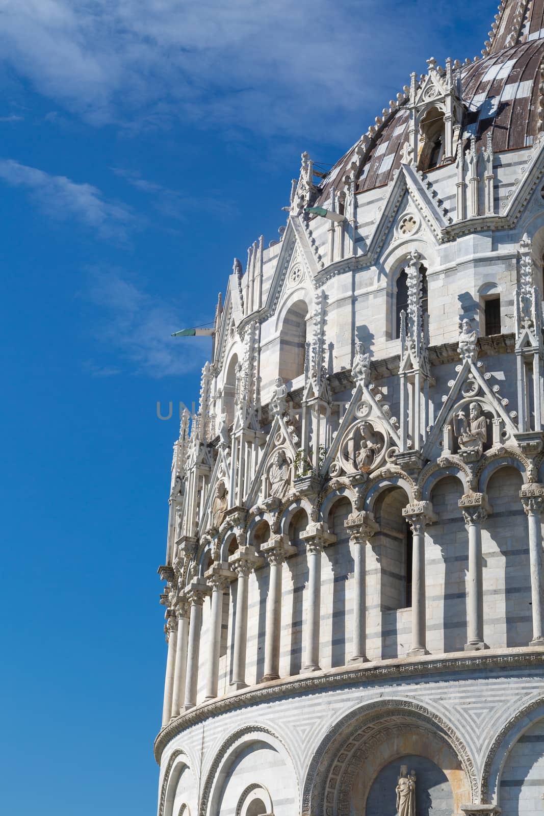 Close up detailed view of Baptisery building in Cathedral Square in Pisa, Italy, on cloudy blue sky background.