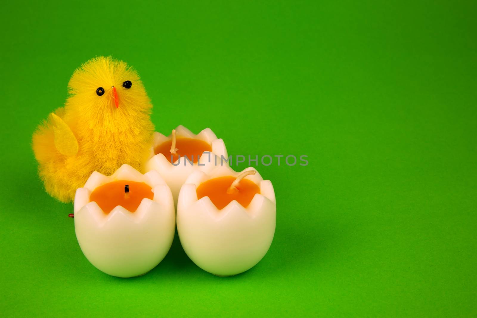 Three easter candle i shape half of eggs and two gigurines yellow chicken on isolated green , easter decoration.
