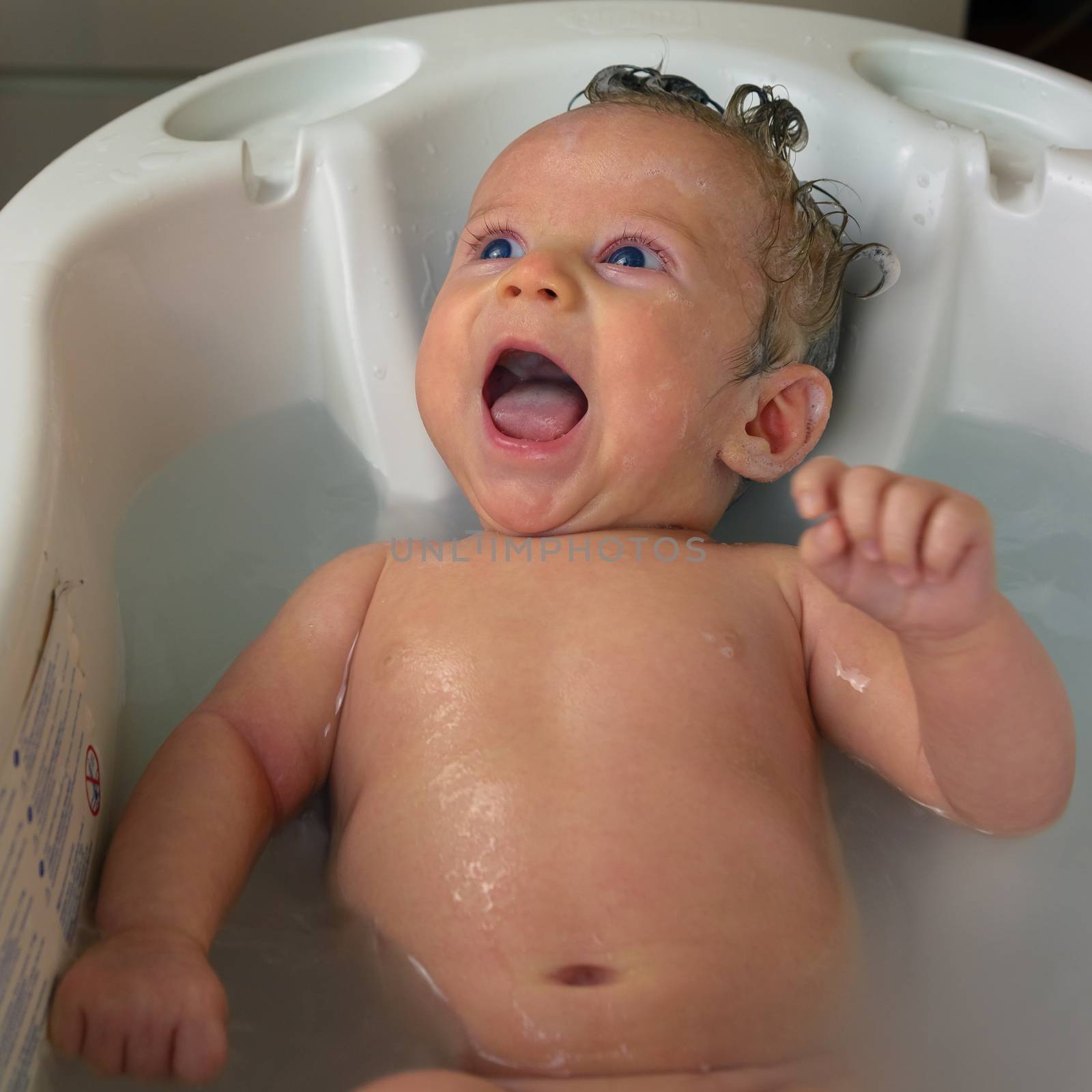 Newborn smiling while taking bath with foam and shampoo