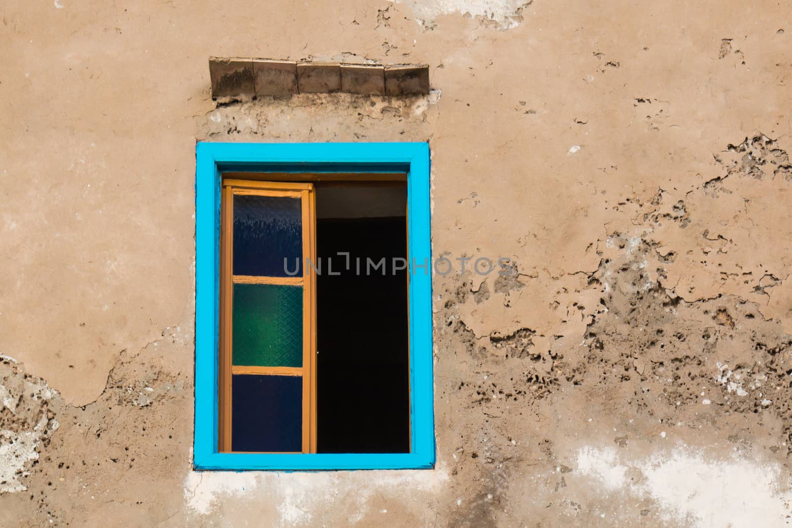 Brown facade of a old house with an opened window with a bright blue frame.