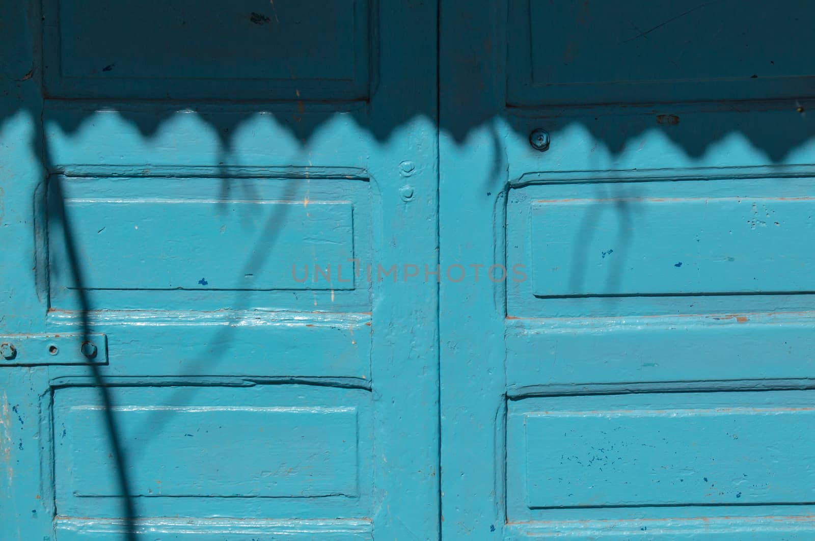 Old blue wooden gate, partly enlightened by sunshine, partly in a shadow created by a blind.