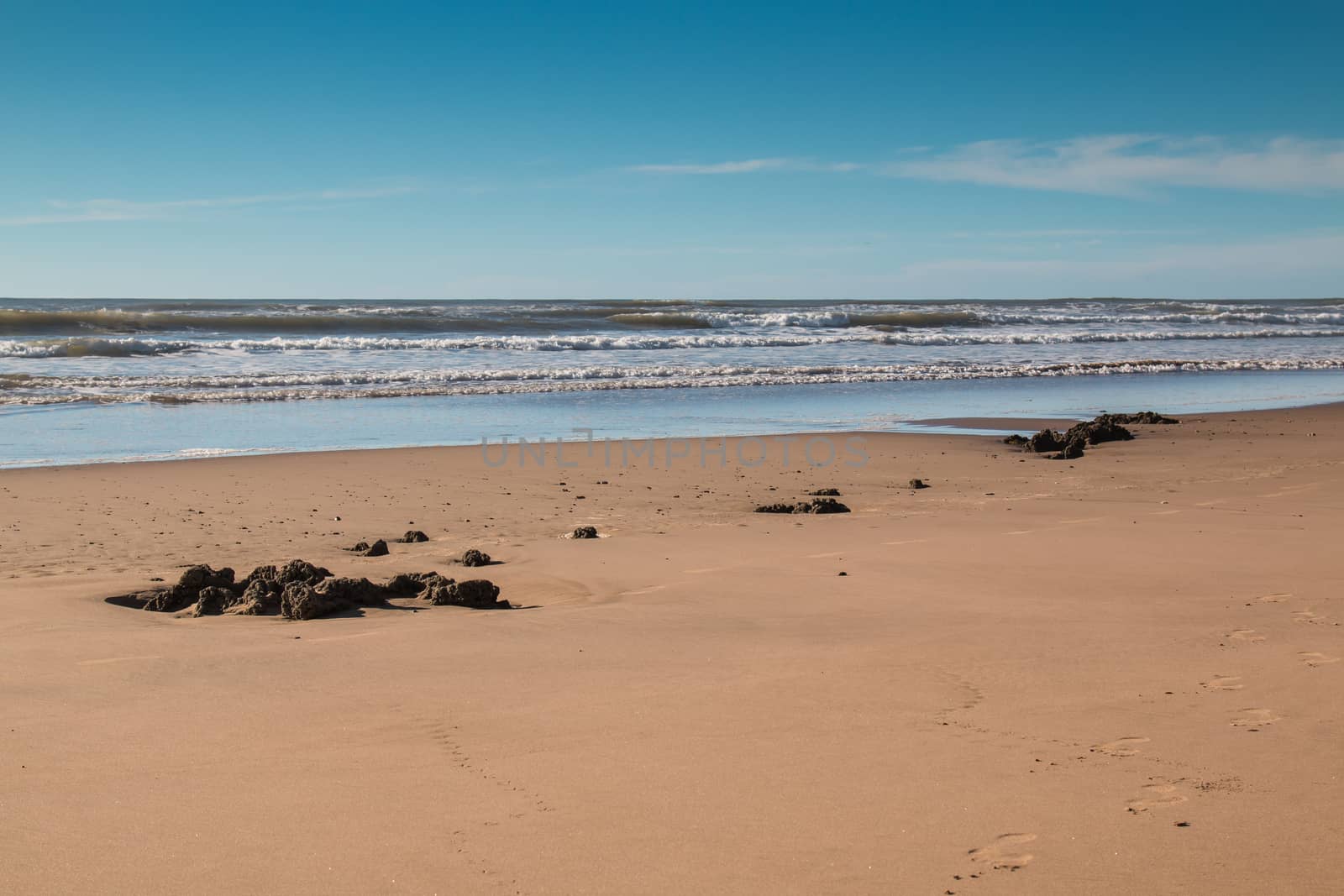 Sandy beach on the Atlantic ocean shore in Morocco. Calm day, just small waves, blue sky with a cloud.