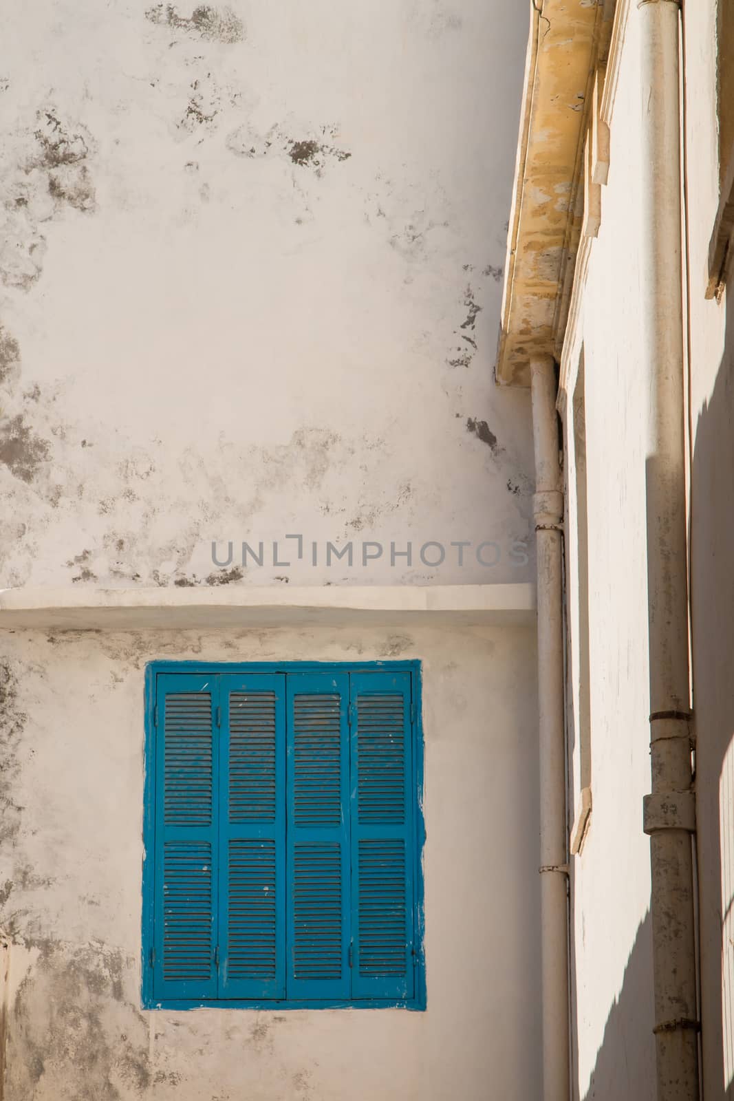 View on the corner of old houses in the city Essaouira in Morocco. Old wall, enlightened by sunshine and a window with blue shutter.