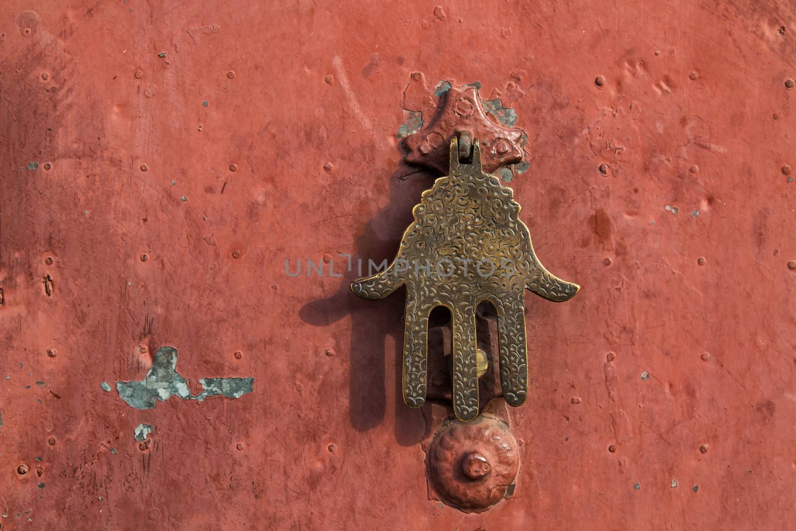 Door in Morocco with an ornamental Fatima hand (Khamsa) thought to give protection against evil, danger, or disease. Orange metal background.