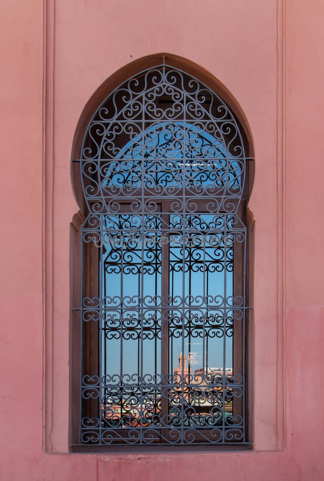 Arch of the traditional arabian window with a reflection of the famous square Jamaa el Fna and a blue sky.