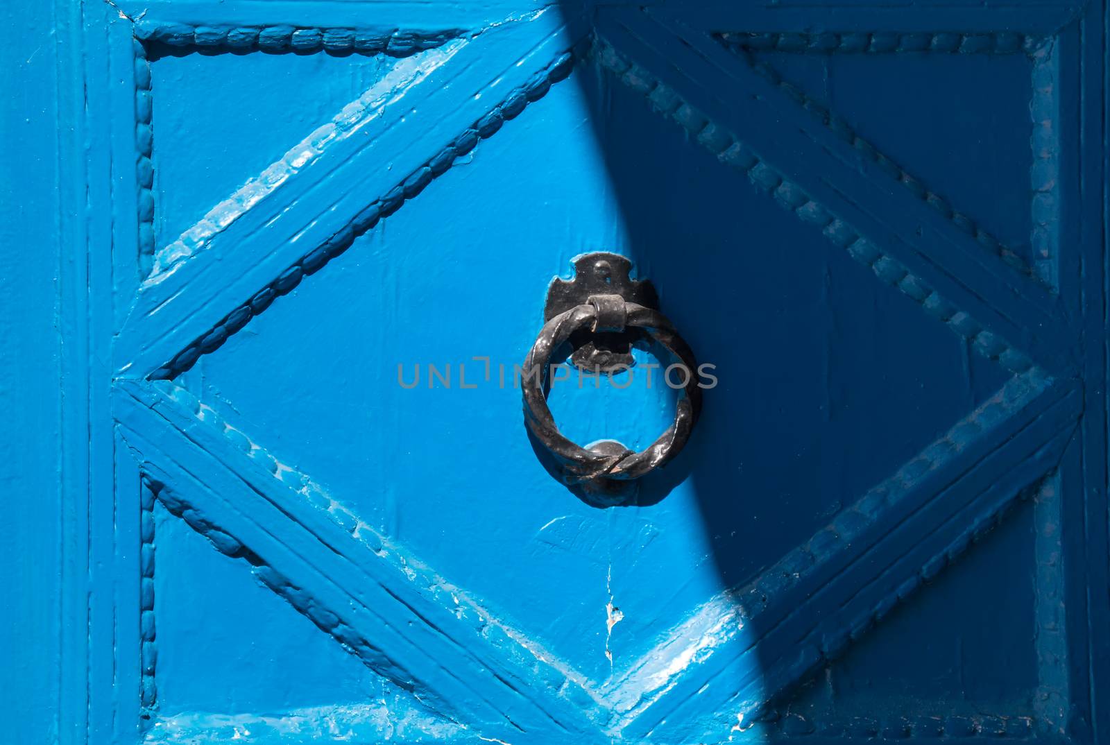 Detail of the blue old wooden door with a round hammer. Divided to sunny a shady part.