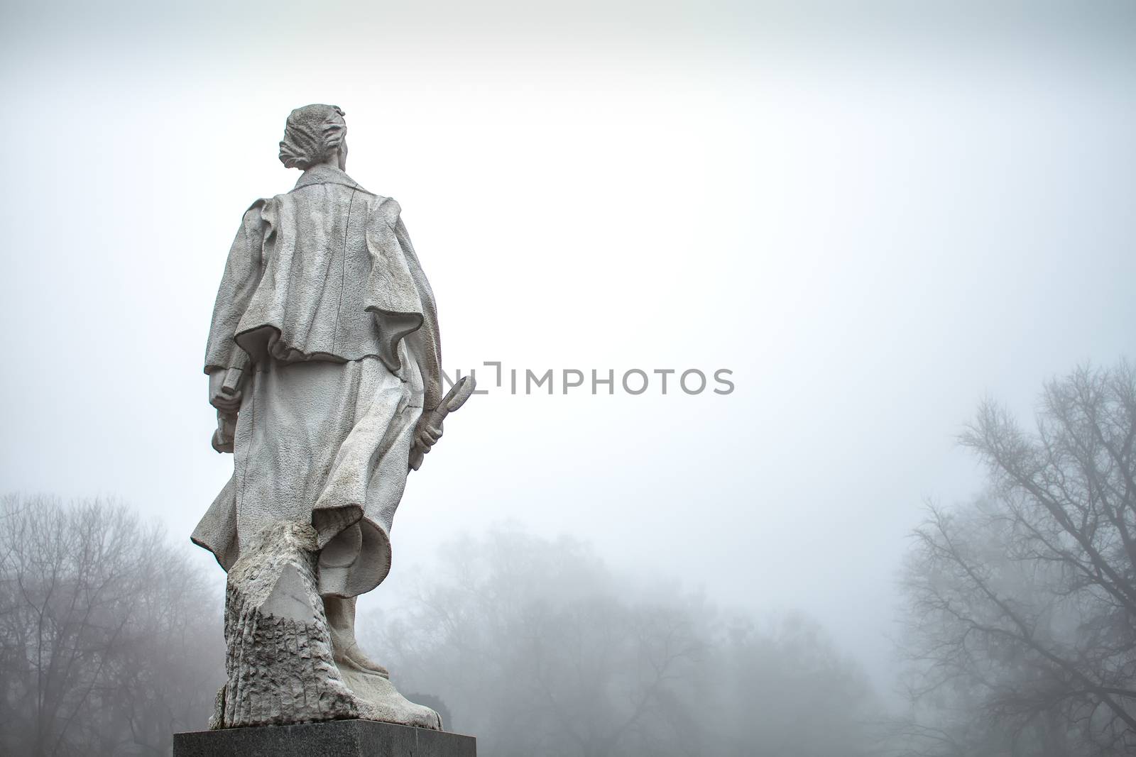 Early morning in the winter after a night rain. Intense fog. Statue of Janko Kral looking forward, trees  without leaves.