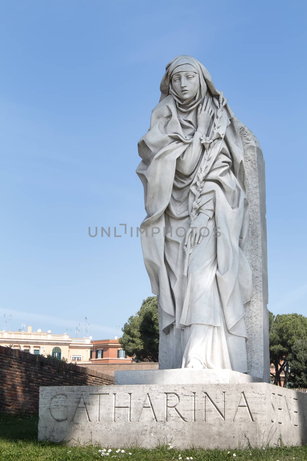 Statue of Catharina in italian Rome. Buildings in the background. Light blue sky.