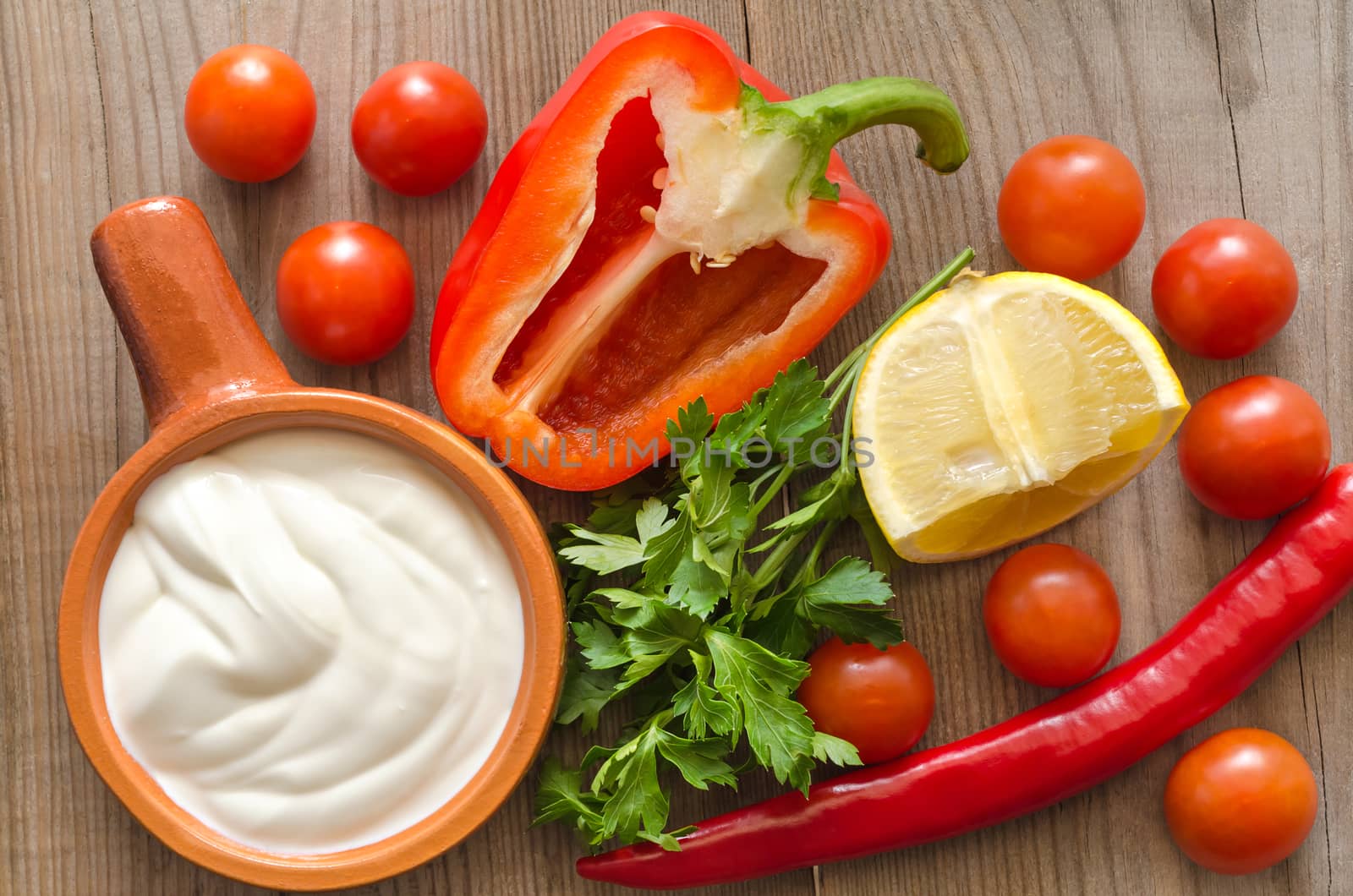 Ceramic dishes with sour cream, and ingredients for salad on an old wooden table.