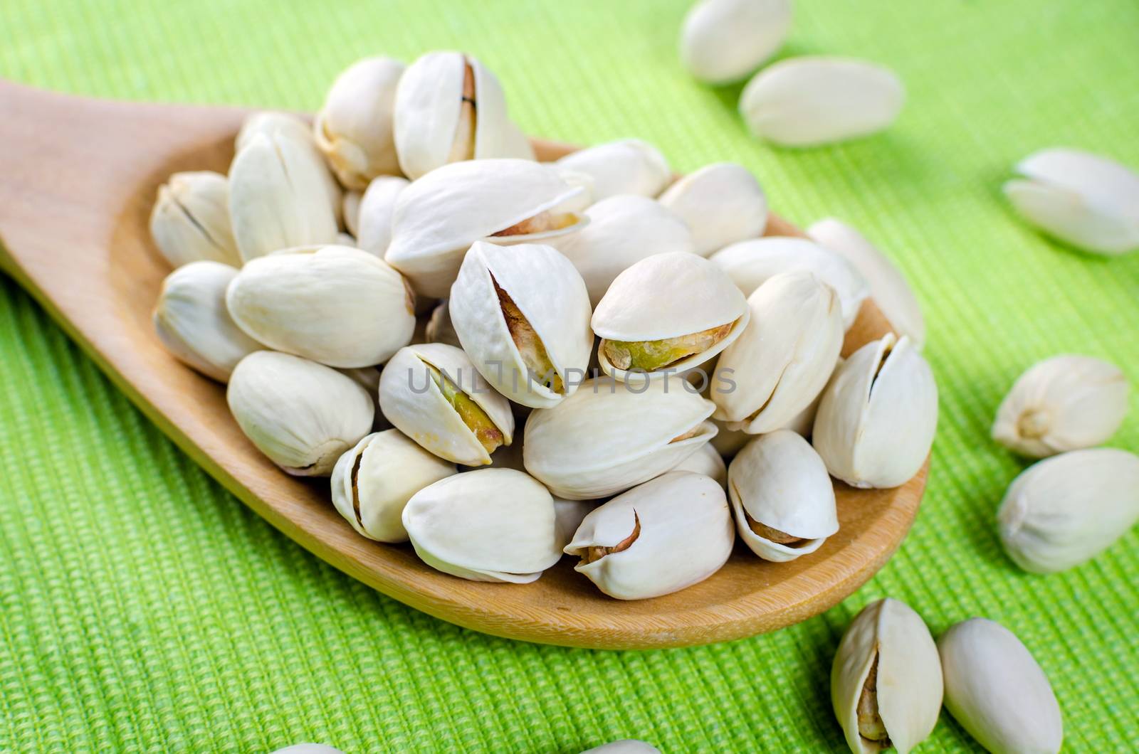 pistachio nuts in a wooden spoon on green background