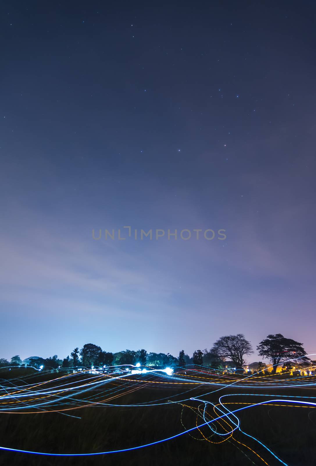 Beautiful Blue dark night sky and stars above field of grass and colorful of light