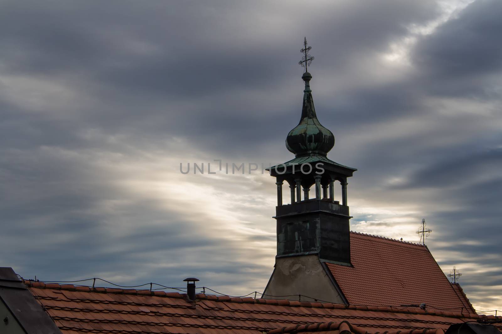 Church of St. Nicolas in Bratislava, Slovakia. Early cloudy rainy morning. Heavy dark clouds broken by a sunshine. Roof in the foreground.