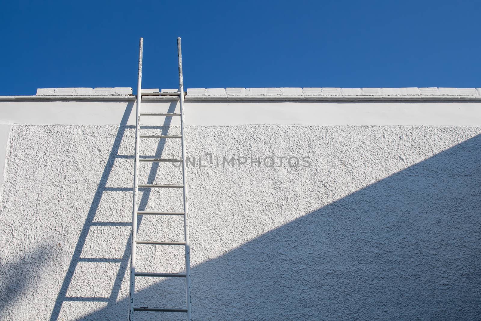 White ladder beside a white wall. Clear blue sky without clouds.