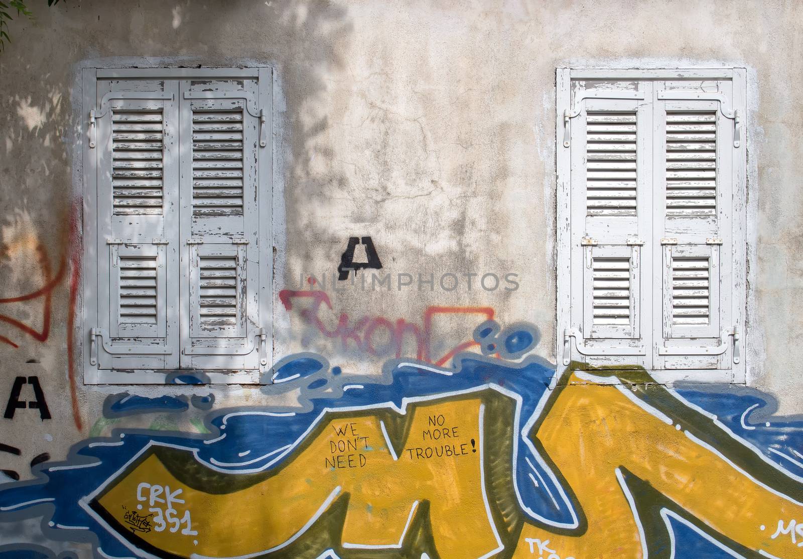 Old windows with a white shutters. Wall of the house with graffiti tags. Athens, Greece.