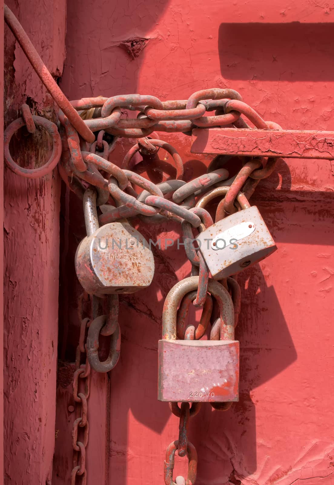 3 old padlocks on the old gate, which is painted red. The padlocks are hanging on a massive chain. — Photo by YassminPhoto