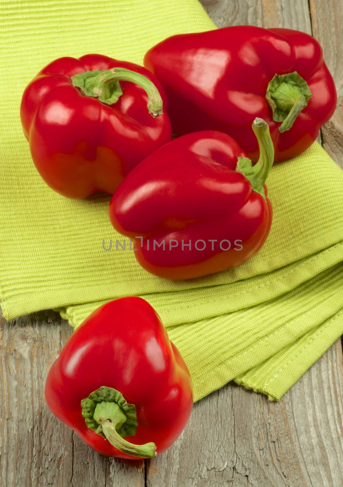 Heap of Four Ripe Red Bell Peppers on Green Napkin closeup on Rustic Wooden background