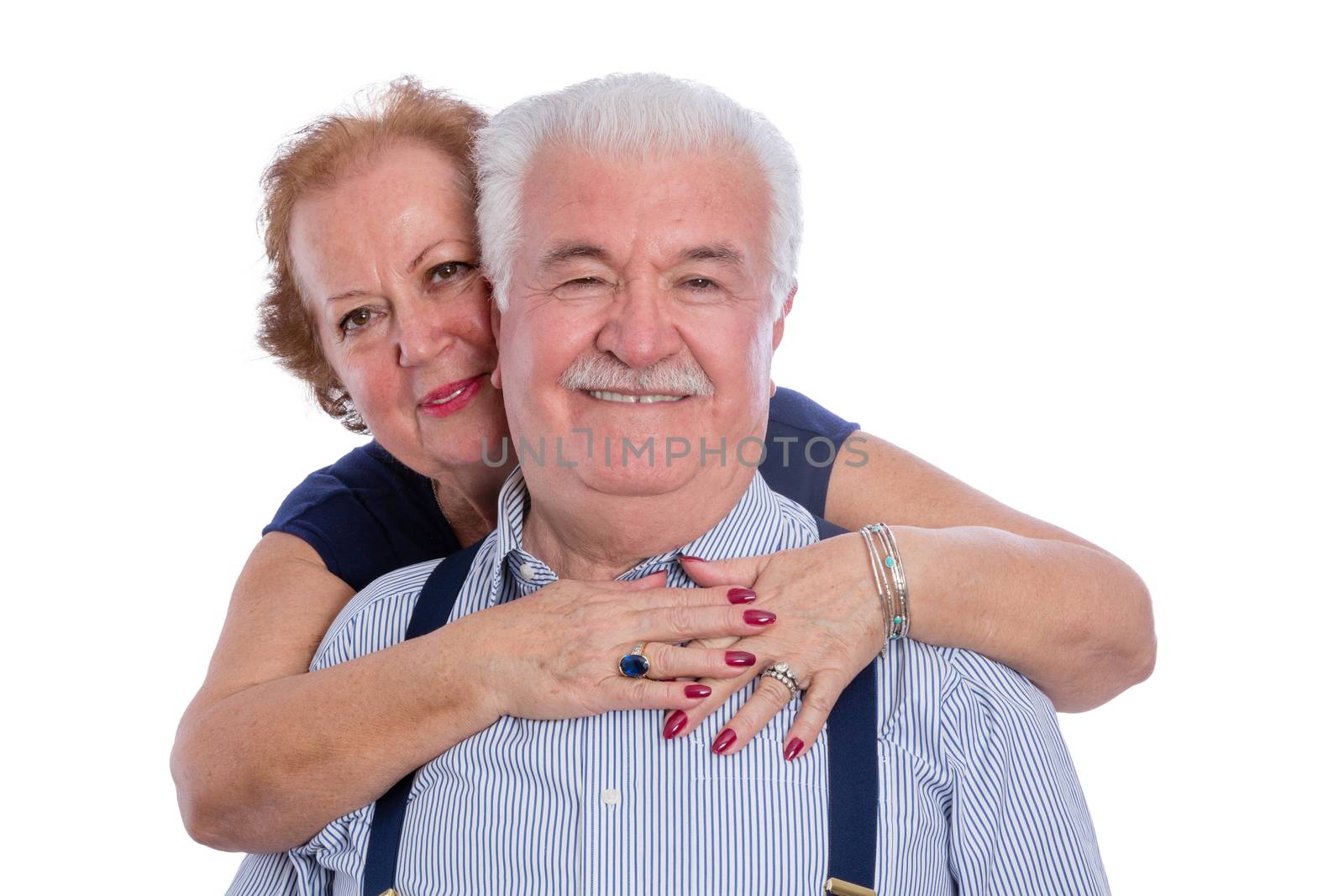 Laughing husband in pinstripe shirt with suspenders being hugged by happy wife over white background