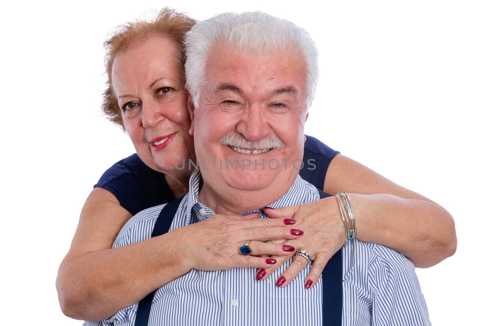 Smiling husband in pinstripe shirt with suspenders being hugged by happy wife from behind over white background