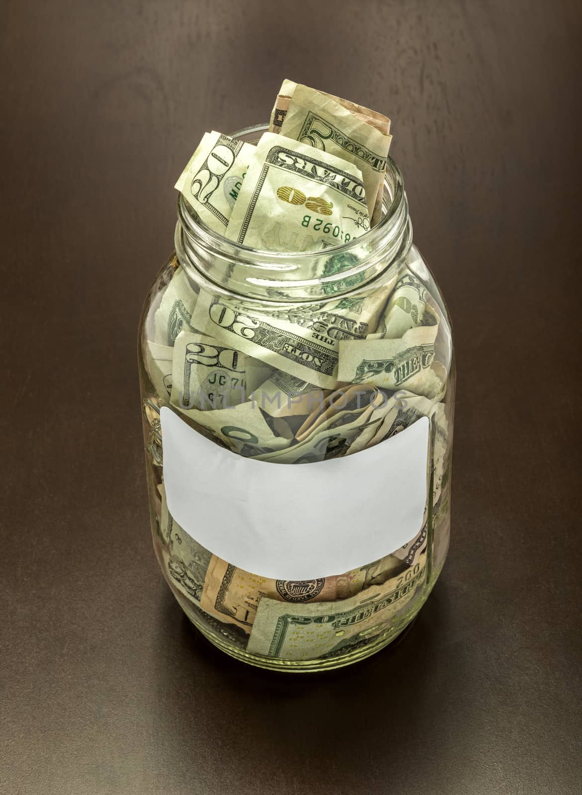 Clear glass cash jar full of money on a brown background.