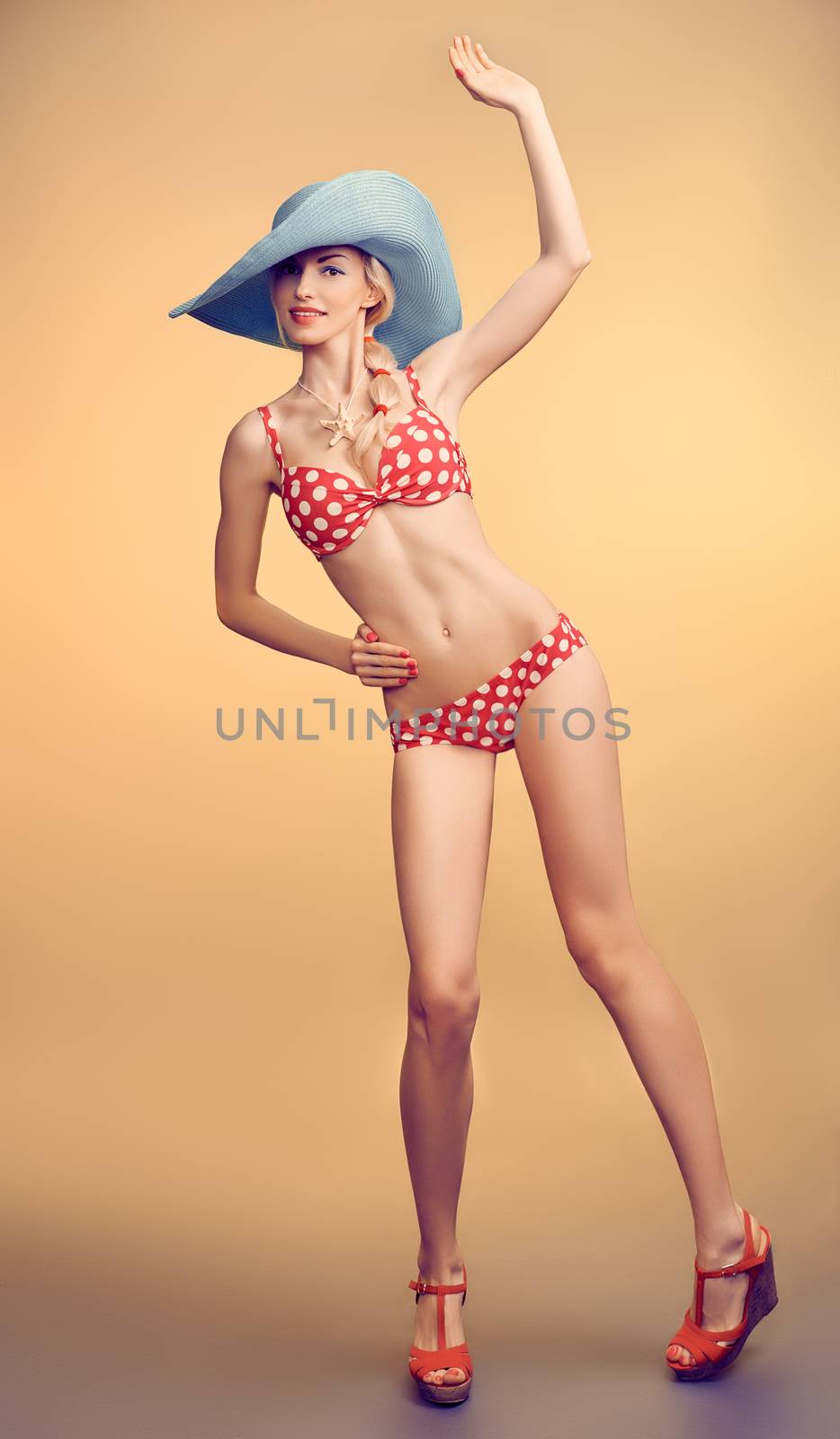 Sexy PinUp woman in fashion red polka dots swimsuit, blue hat, beach slim body. Playful blonde girl in bikini smiling. Summer holiday, sea vacation. Yellow, vintage toned, unusual creative provocative