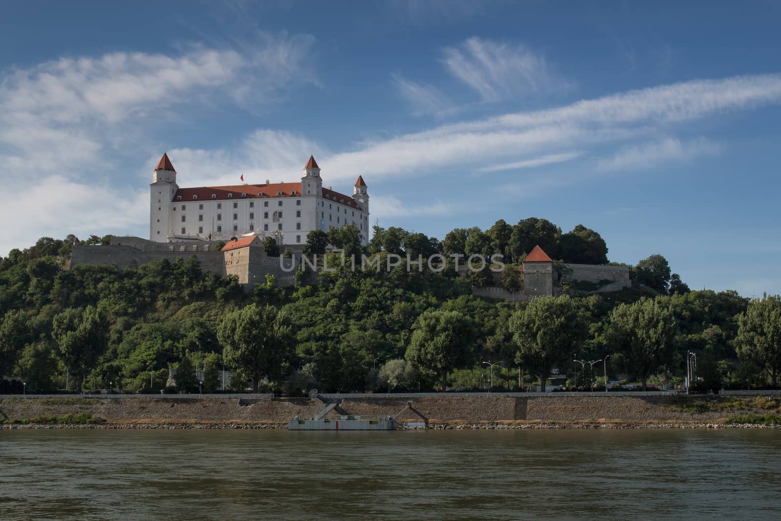 View on a castle in Bratislava, located on the top of the hill. River Danube in the foreground. Blue sky with white clouds.