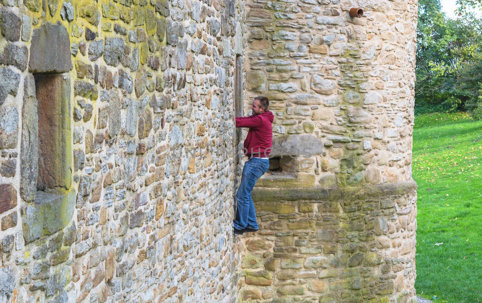 Young Adult Man climbs up a castle wall.