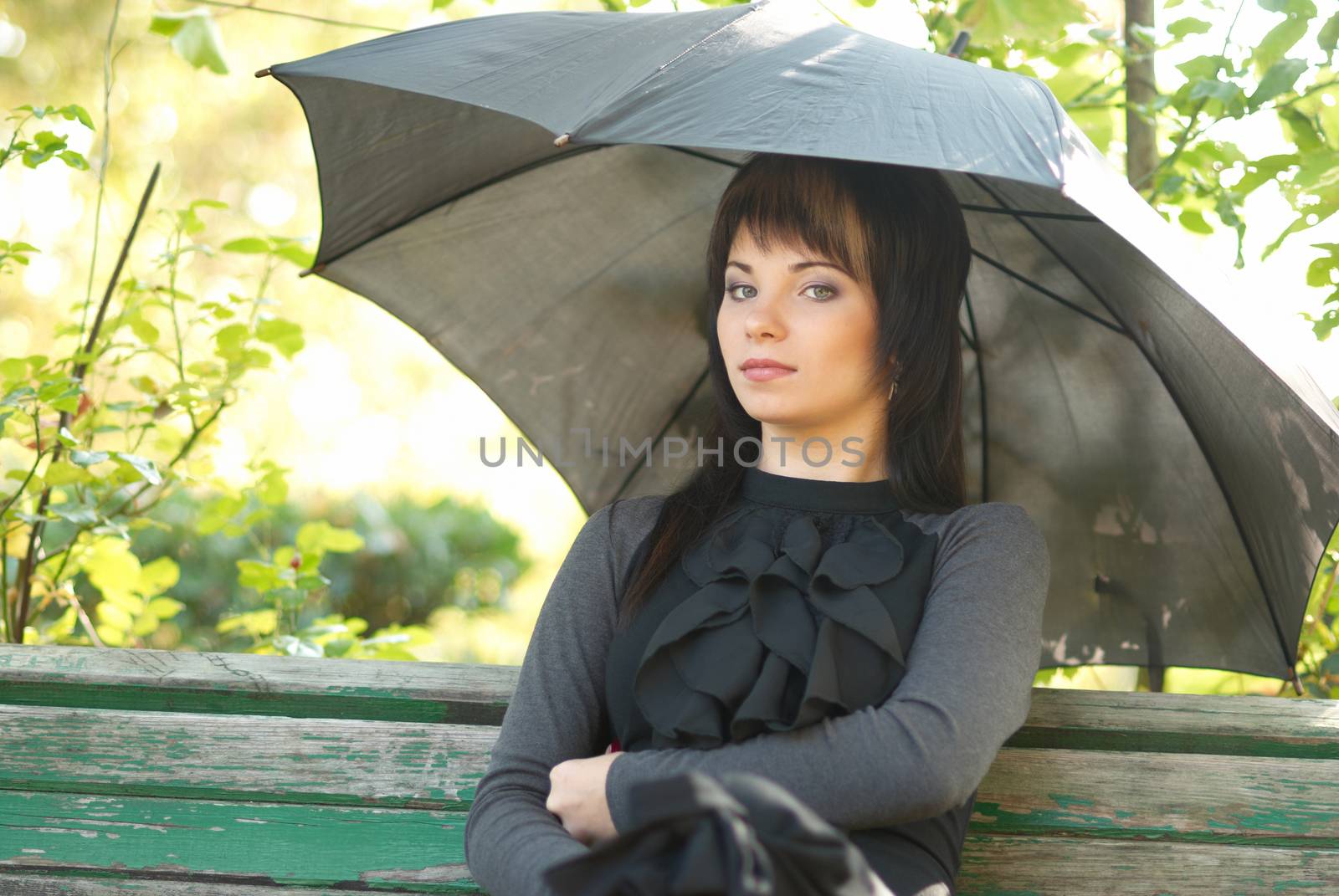 Portrait of beautiful girl with umbrella sitting in the park