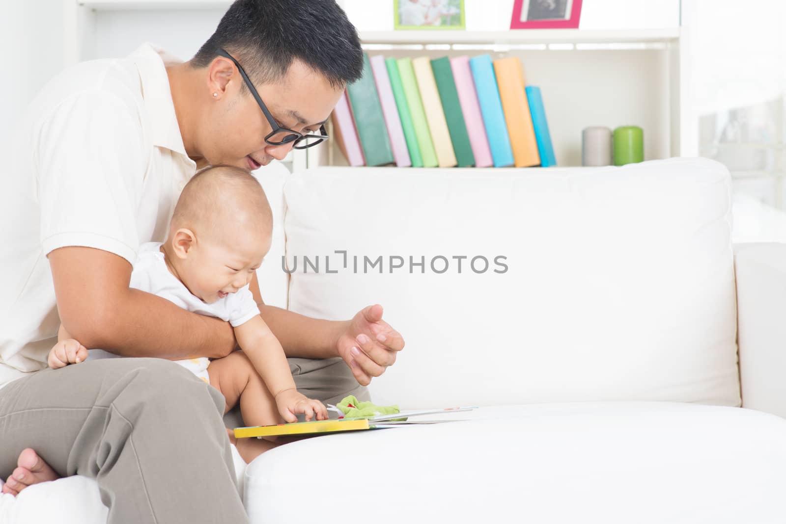 Asian family lifestyle at home. Father and child reading story book on sofa.
