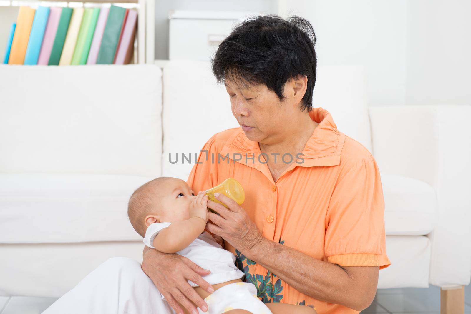 Nanny taking care baby at home. Feeding solid food fruit puree with bottle.